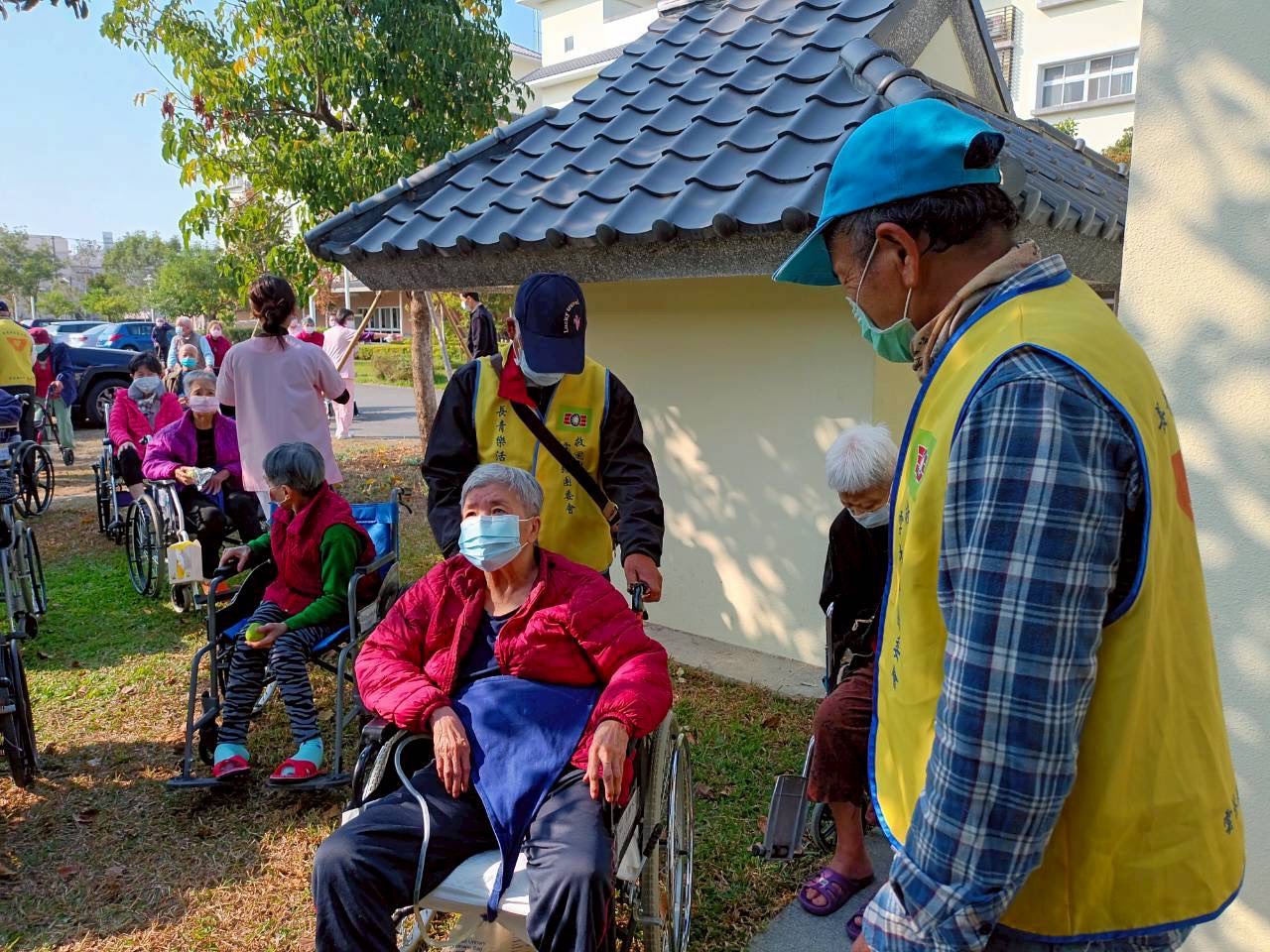 志工推著輪椅陪伴長輩漫步果園小徑,感受戶外陽光與自然氣息。