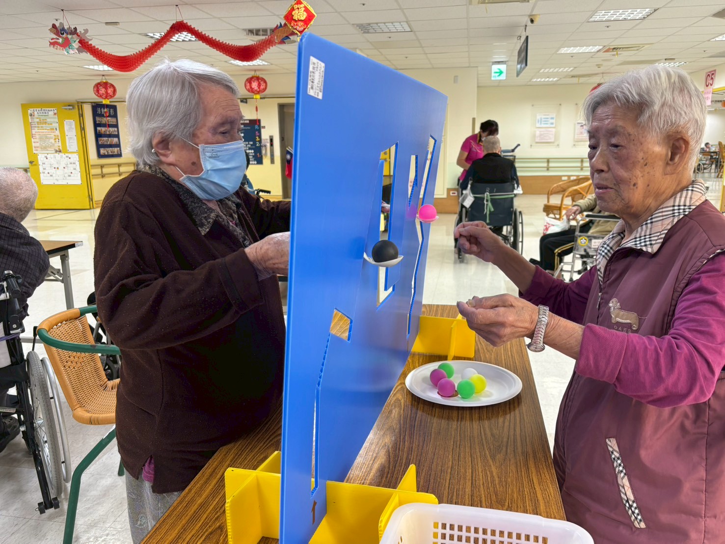 兩位長輩分別站在活動板兩側合作完成任務,透過觀察讓小球順利通過關卡。活動不僅訓練手眼協調與反應能力,也增進長輩之間的互動交流。