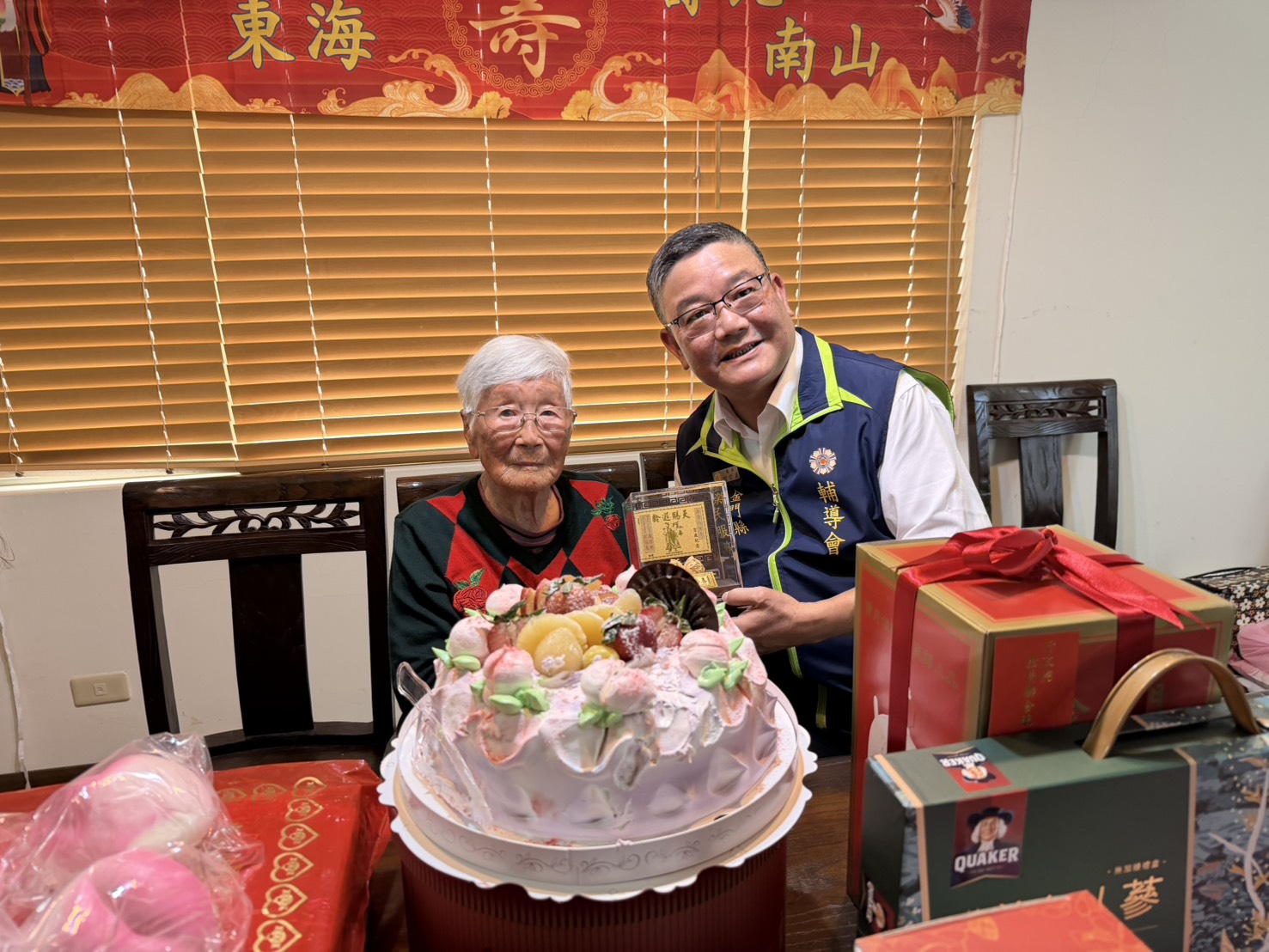 圖一劉信義處長(右)代表主任委員嚴德發致贈壽星李許八奶(左)金壽桃