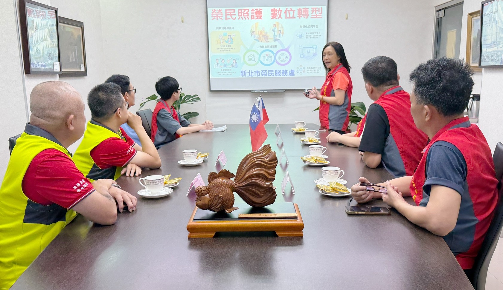 新北市榮民服務處王玟琳組長(站立者)向中華民國榮光地產聯合服務協會林建榮理事長(左一)、許裕旻秘書長(左二)介紹輔導會「安心御老平台」專案。