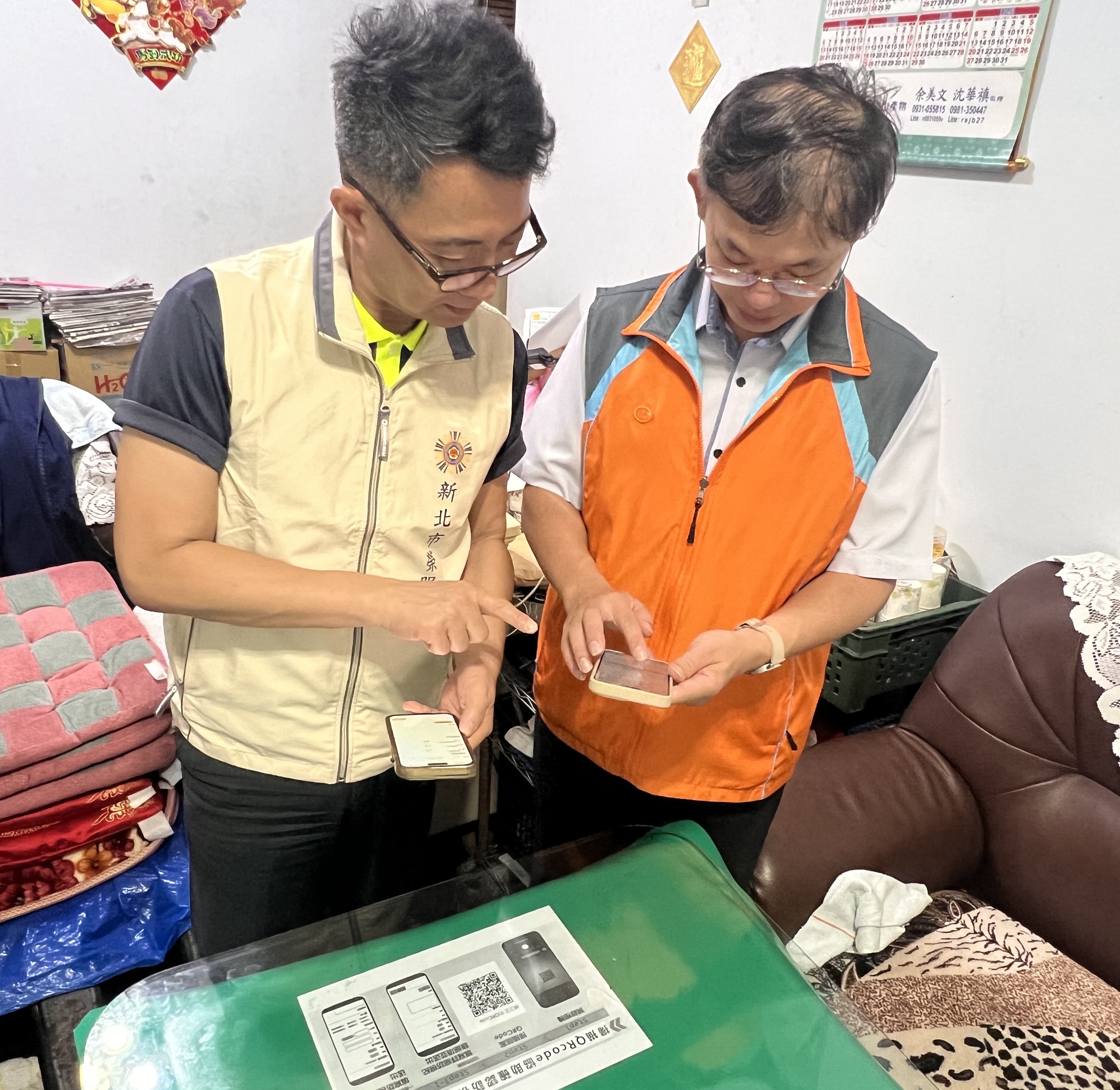 陳處長(左)偕同板橋郵局陳股長(右)掃描輔導會與中華郵政公司合作辦理「獨老關懷」QR Code,登入安心御老系統完成訪視打卡。