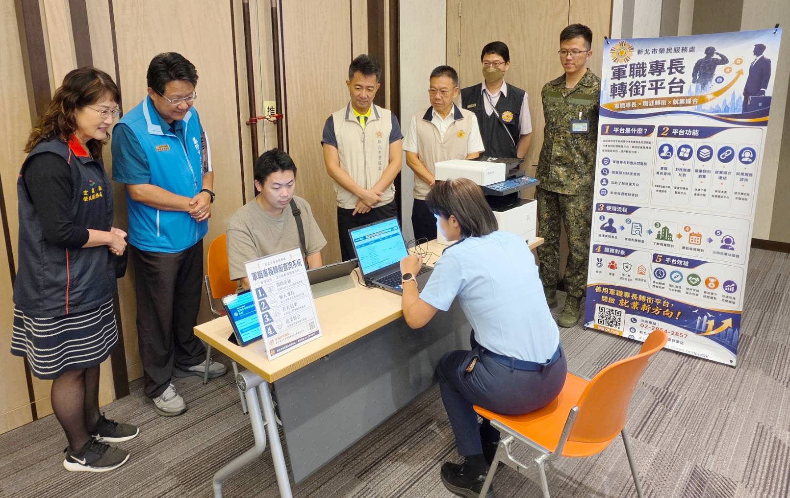▲新北市榮服處於活動現場設置「軍職專長轉銜服務區」,協助屆退官兵盤點軍中專長,對接民間職務及產業需求。陳立中處長(後排立者左3)、李建學專門委員(後排立者左4)實地瞭解平臺操作情形。/新北市榮服處提供