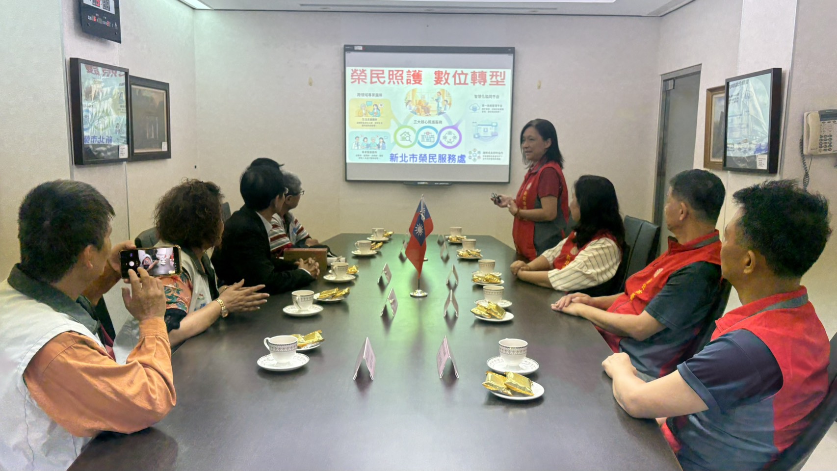 ▲王玟琳組長(立者)向大中華及新北市記者友好交流協會幹部簡報說明輔導會「安心御老」平台、AI就業智能服務及軍民專長轉銜等近期政策。