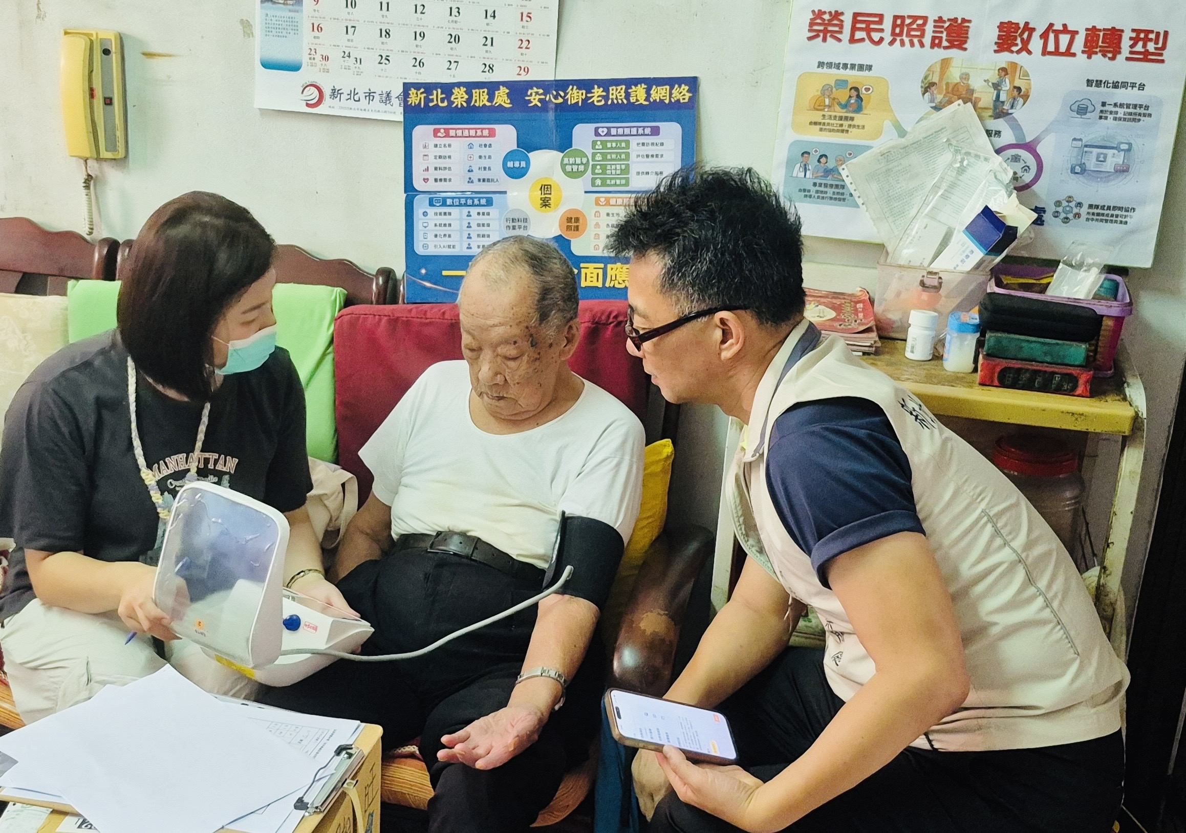 ▲處長陳立中(右)陪同北榮個管師李欣慈(左)關懷羅伯伯(中)健康,協助量測血壓,專業細心。/新北市榮服處提供。